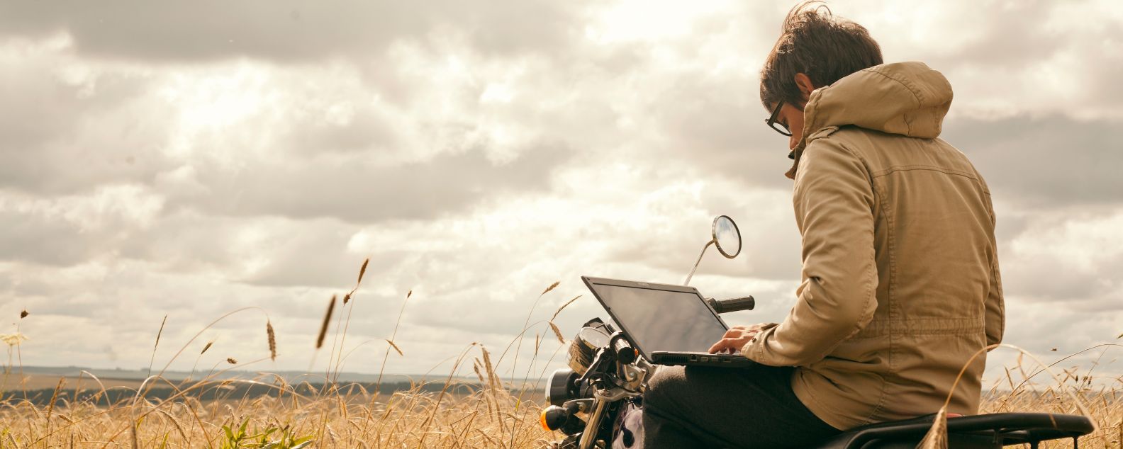 Person sitting on motorcycle while working on a laptop computer
