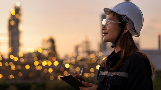 Un ingénieur en raffinerie de pétrole, dans l'industrie pétrolière et gazière, portant un EPI de sécurité pour une inspection, vérifie sa liste de contrôle sur une tablette