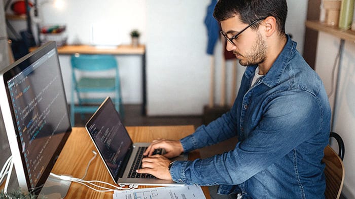 Sideview of a man working on a computer with external monitor at a desk