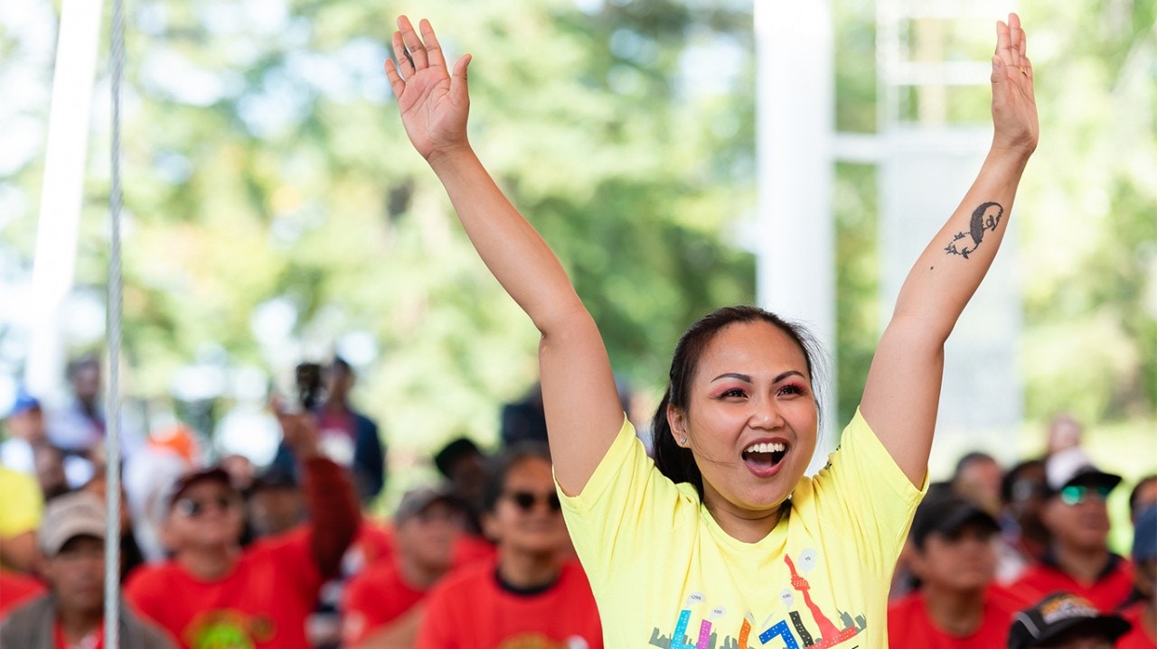 Mujer frente a una multitud animando con los brazos levantados