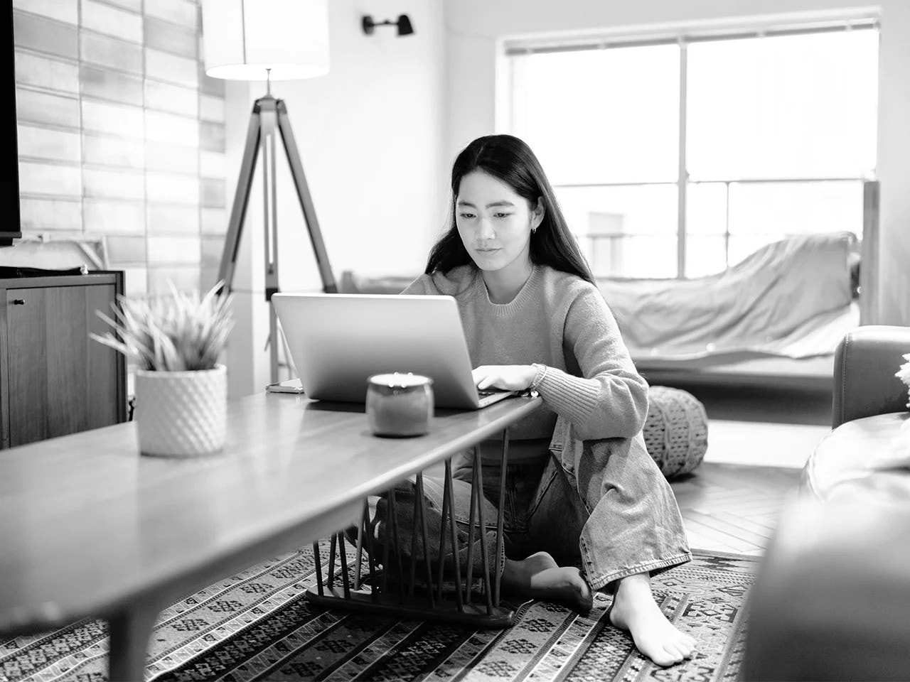 Person sitting on floor rug at table in home working on laptop 