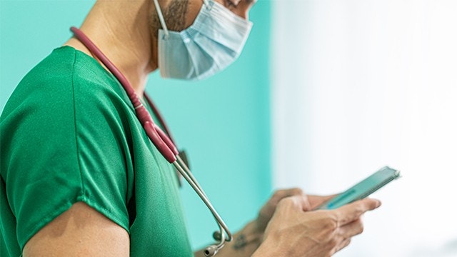 戴着面具的男护士正在使用智能手机