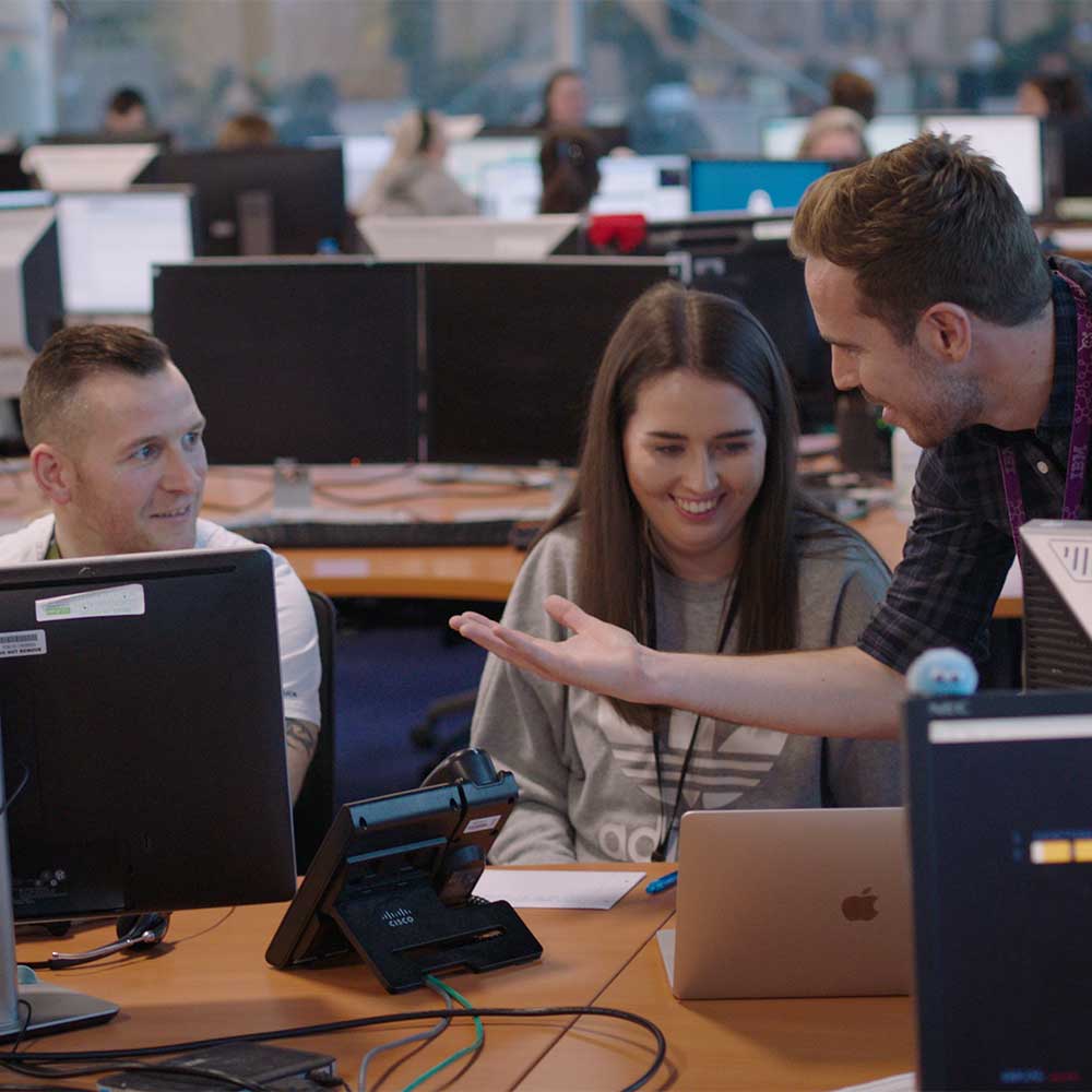 Équipe de collègues discutant et souriant autour d’un ordinateur