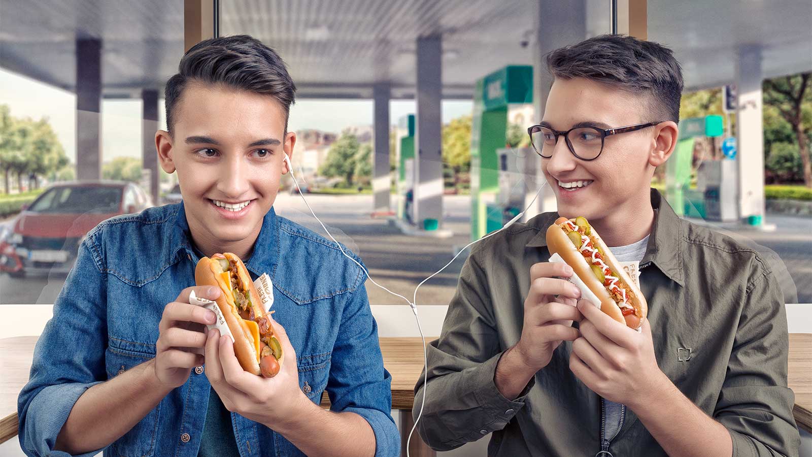Deux adolescents partageant des écouteurs et mangeant des hot-dogs dans une station-service