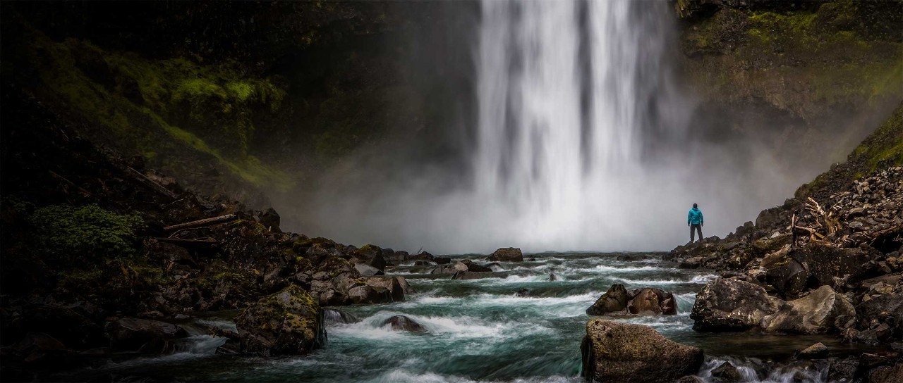 Person in den Bergen, die einen Wasserfall betrachtet