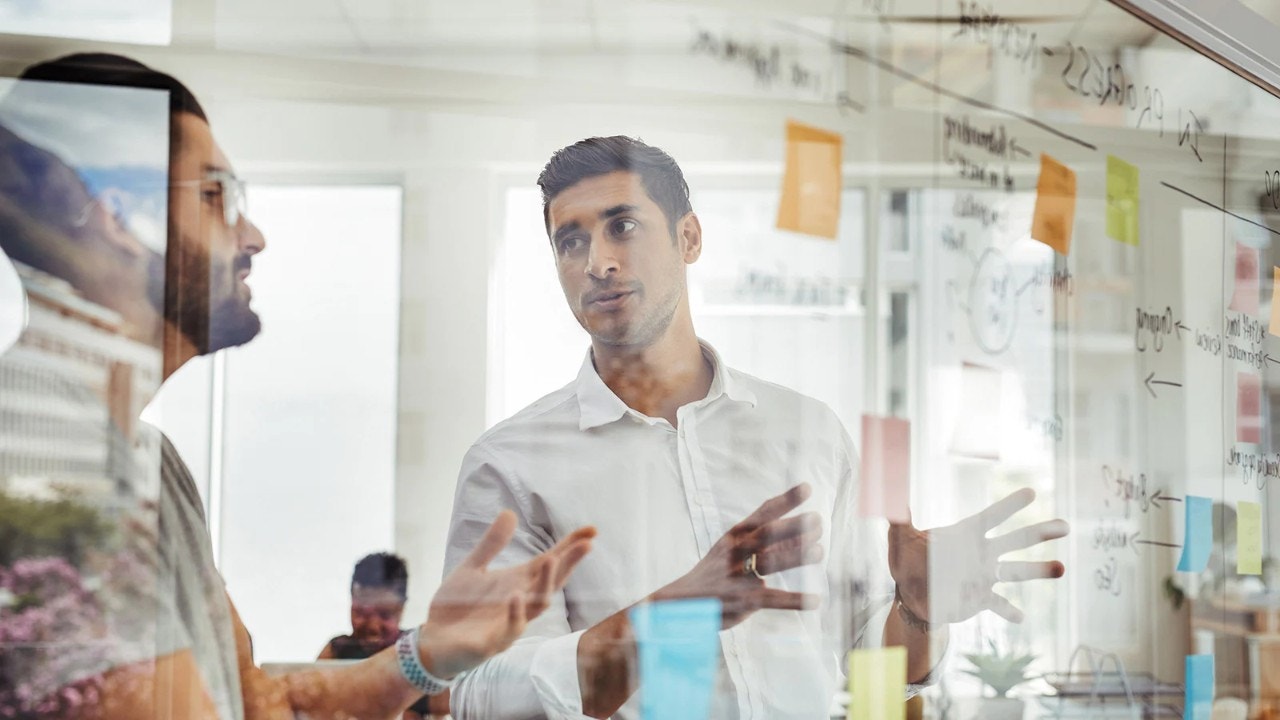 Dua orang berunding di depan papan kolaborasi