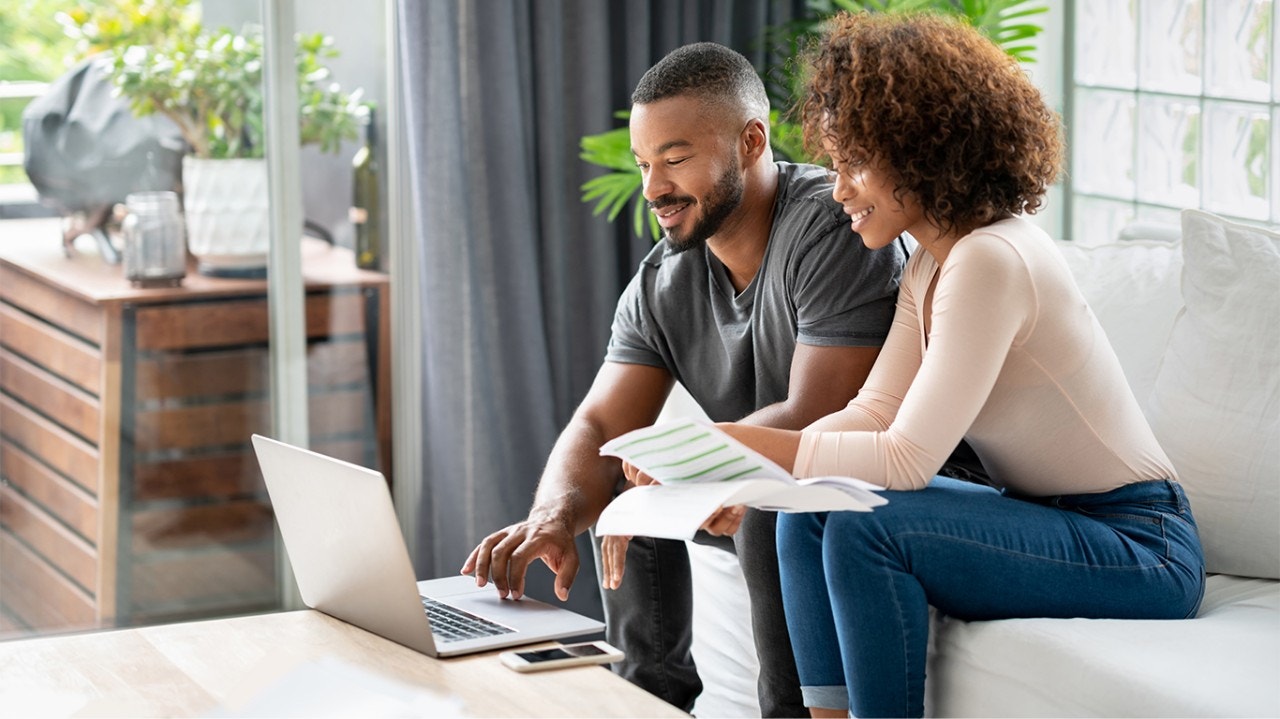 A couple paying bills online at home using a laptop computer and smiling
