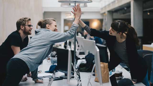 Pemrogram komputer wanita yang bahagia melakukan tos di atas meja di kantor