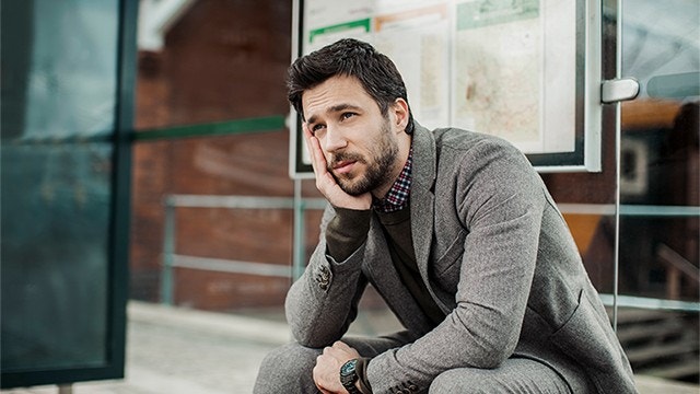 Tired businessman sitting in a bus shelter