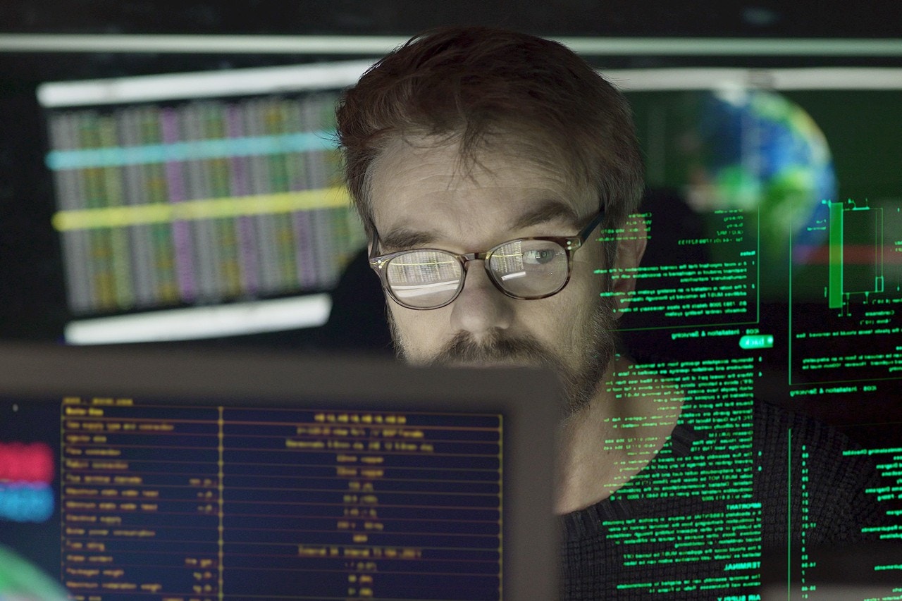 Gros plan sur un homme d’âge mûr entouré d’écrans avec superposition de caractères qu’il est en train de lire.