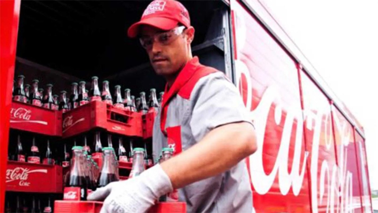 Homme dans un uniforme Coca-Cola sortant des canettes Coca-Cola d’un camion Coca-Cola