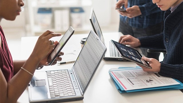 Um grupo de colegas de trabalho realizando uma reunião usando notebooks, dispositivos móveis e tablets digitais