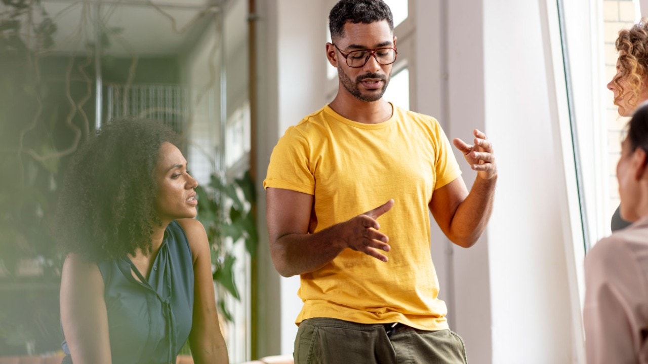 Jeune homme en chemise jaune et portant des lunettes discutant avec trois collègues