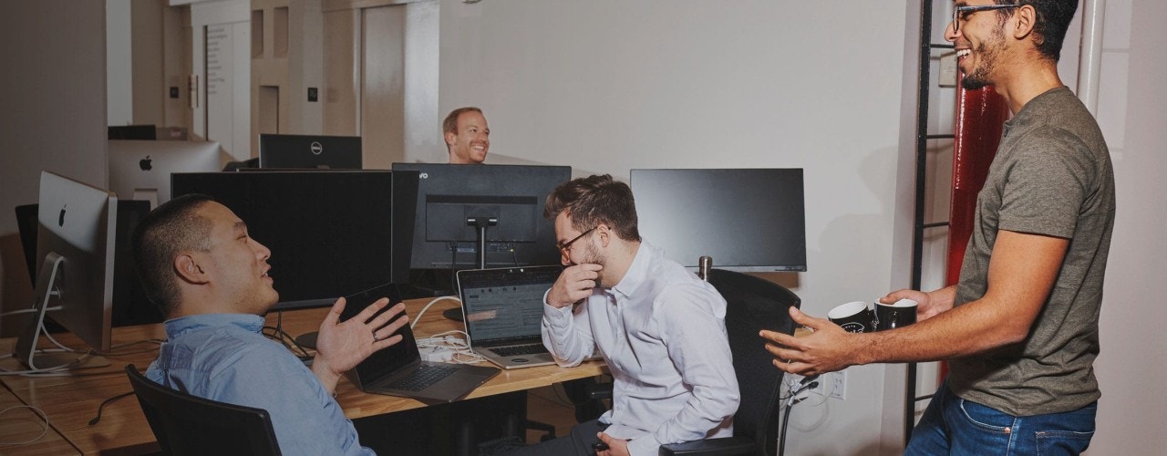 Des employés de bureau riant et discutant assis à leur bureau partagé