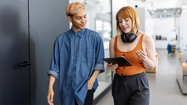 Parceiros de negócios andando pelo corredor do escritório usando tablet digital e discutindo algo do trabalho.