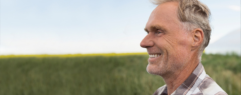 A smiling man looks over green farmland