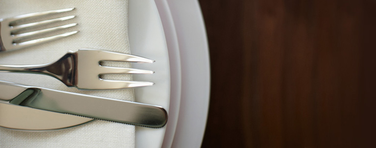 Forks and knives sit atop napkins and plates on a table