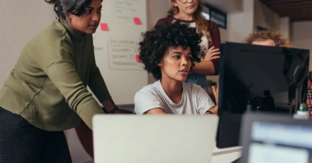 Tres personas reunidas alrededor de un escritorio mientras una persona escribe en un teclado