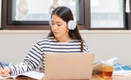 Woman with headphones on laptop taking notes