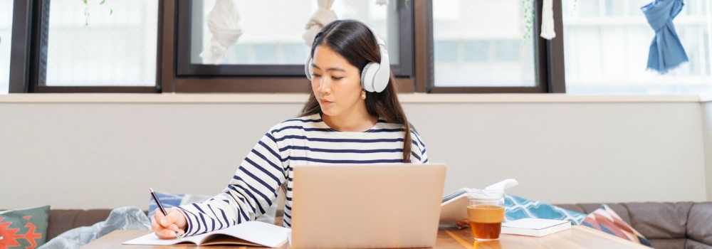 Woman with headphones on laptop taking notes