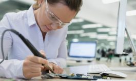 Woman sitting at a desk working on a circuit board with a soldering gun.