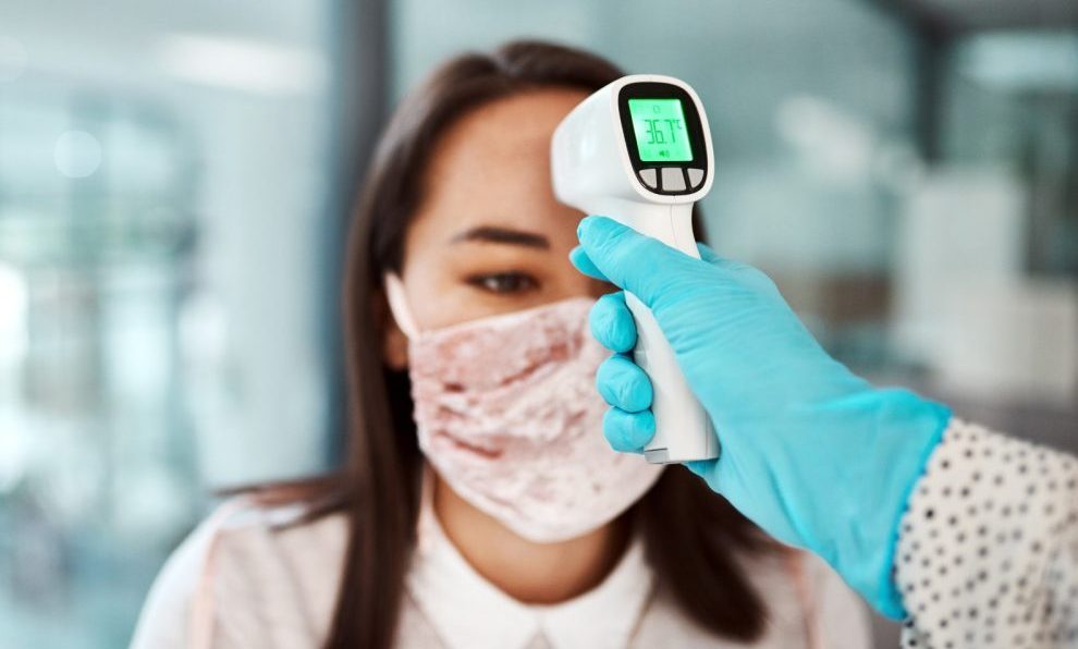 Shot of a young businesswoman getting her temperature taken with an infrared thermometer in an office