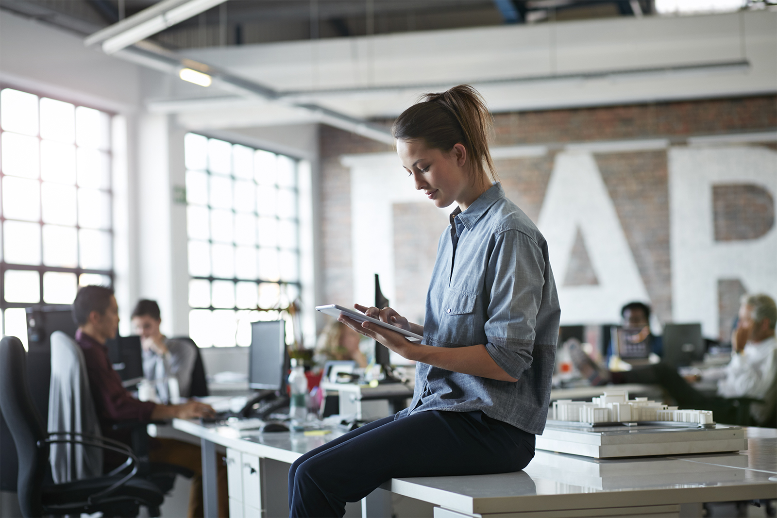 Mujer sentada en un escritorio con una tablet en una oficina abierta