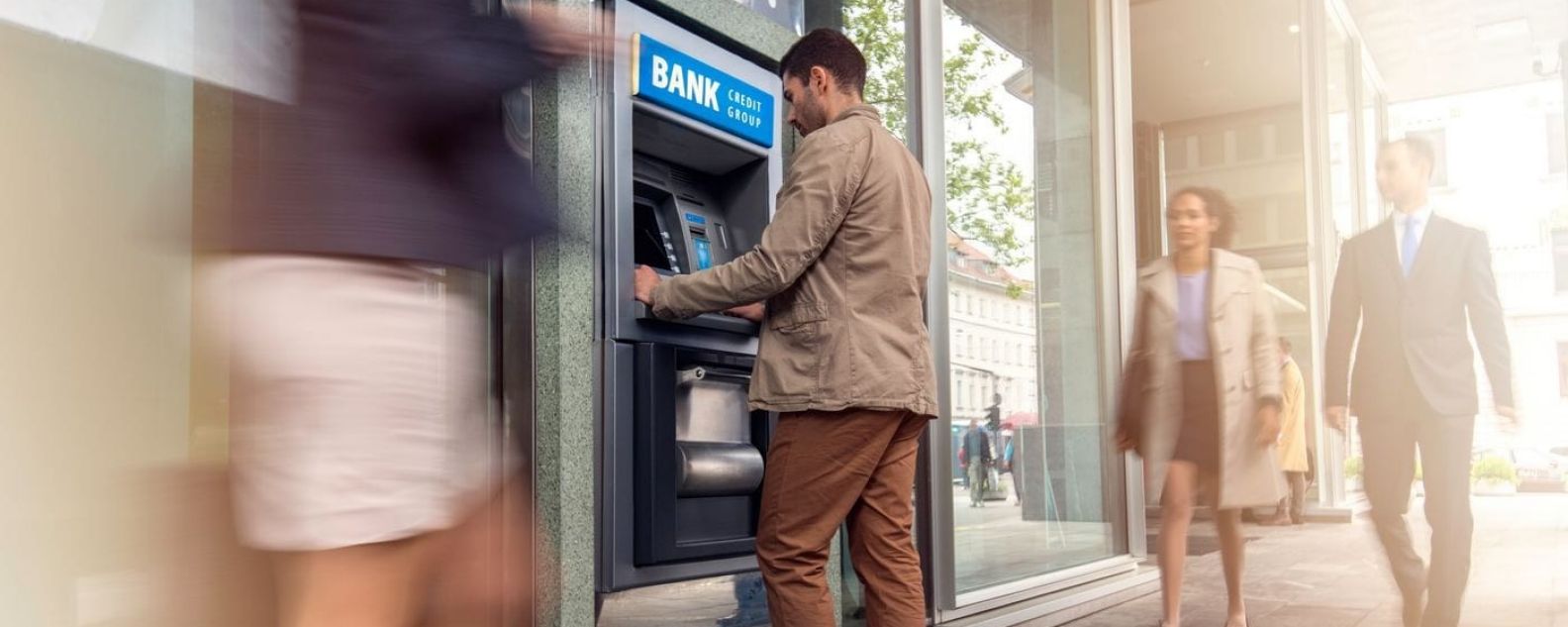男子在繁忙的城市人行道上使用 ATM 机的侧视图