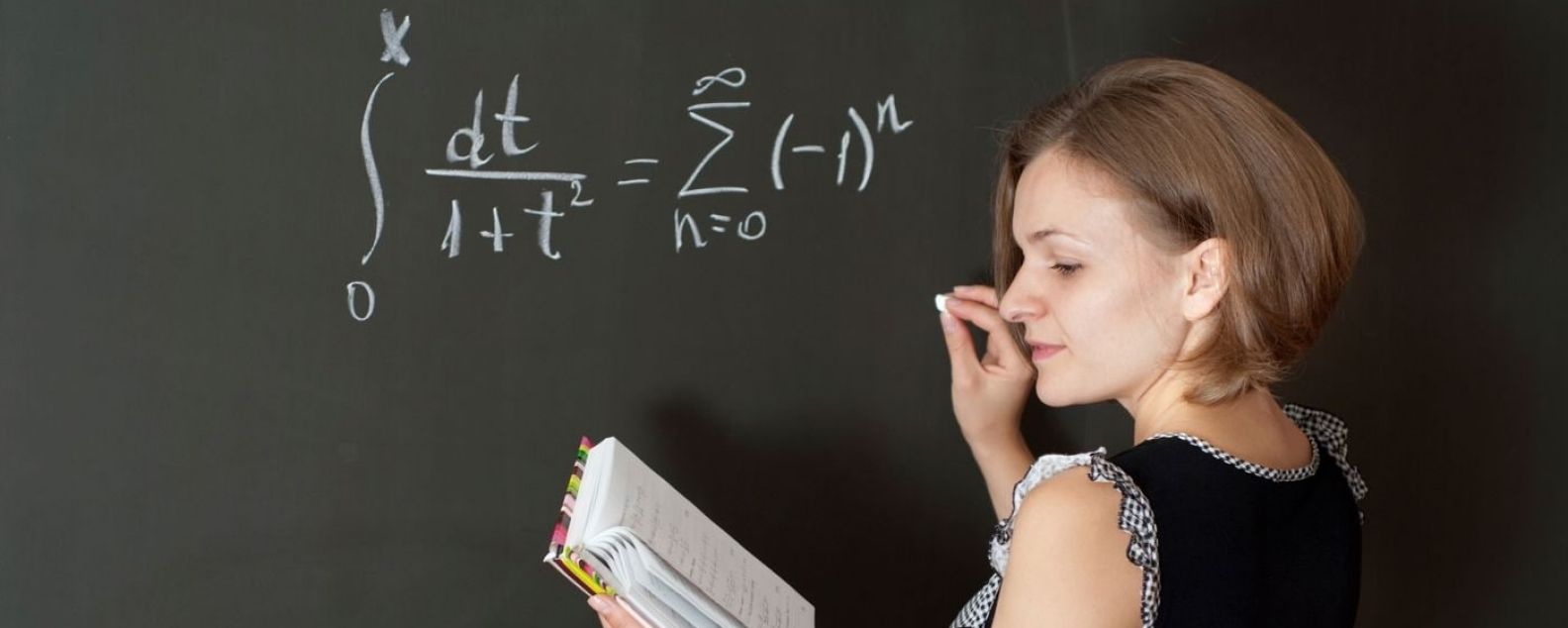 Mujer escribiendo una ecuación matemática en una pizarra mientras hace referencia a un libro