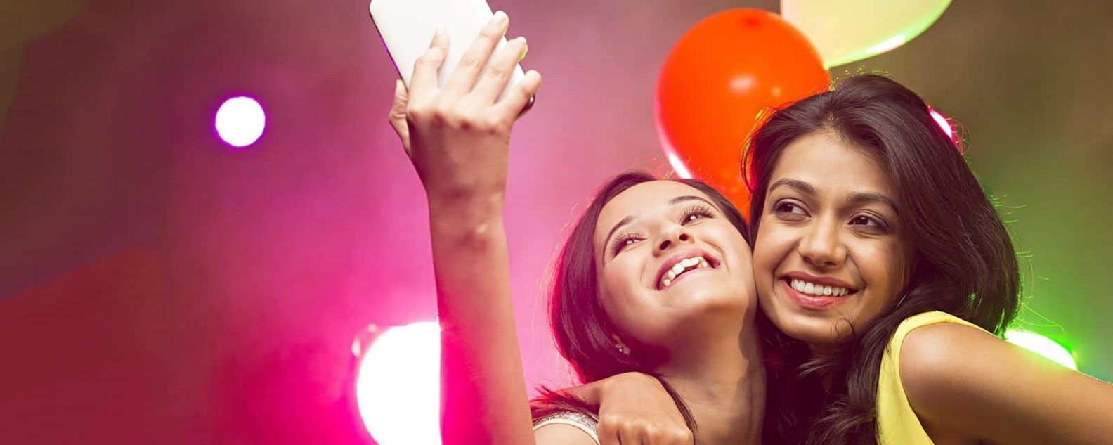 Duas lindas mulheres tirando selfie com uma celebração de festival ao fundo