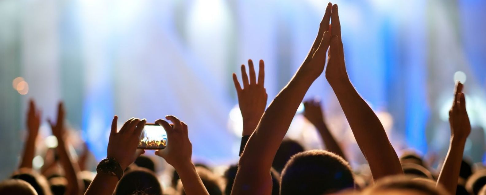 Blick von hinten auf eine Menschenmenge bei einem Konzert mit erhobenen Händen in der Luft