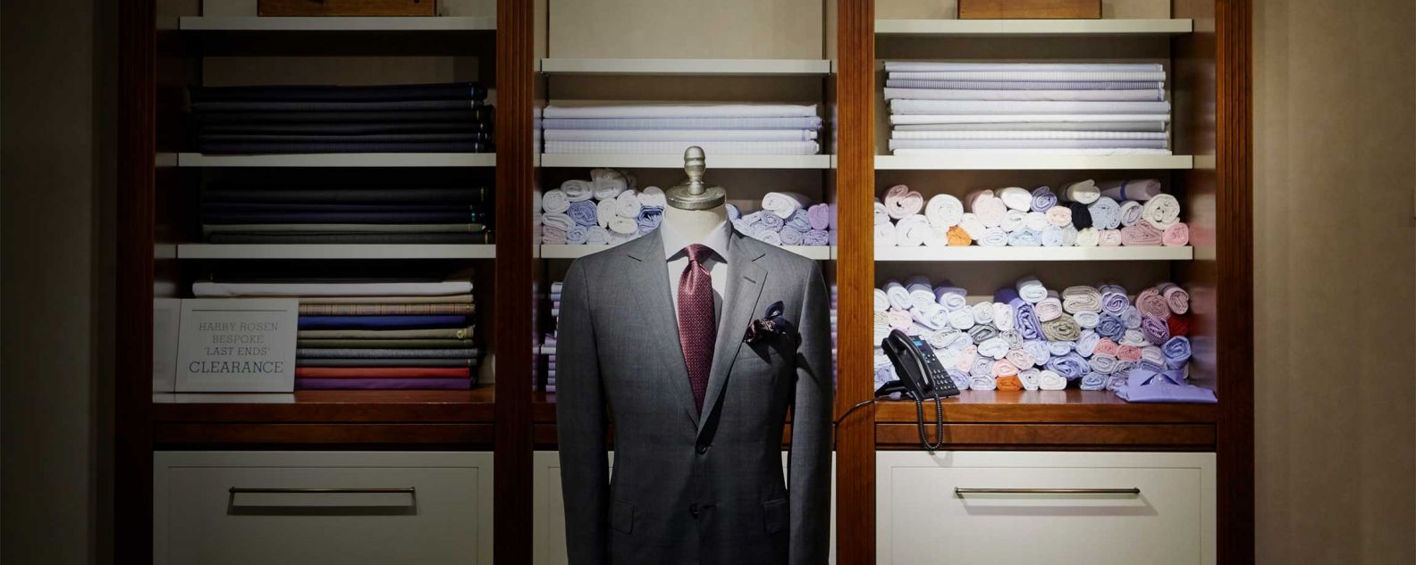 A tailor shop showing a dress suit on a mannequin and shirt fabrics on shelves in the background