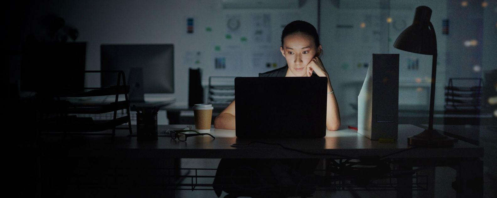 在一个黑暗的房间里，一名女性在笔记本电脑上专心致志地工作