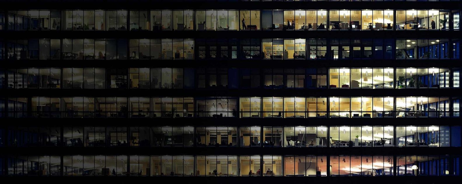 Foto jarak dekat beberapa jendela dan orang-orang yang bekerja di beberapa kantor dari sebuah gedung besar