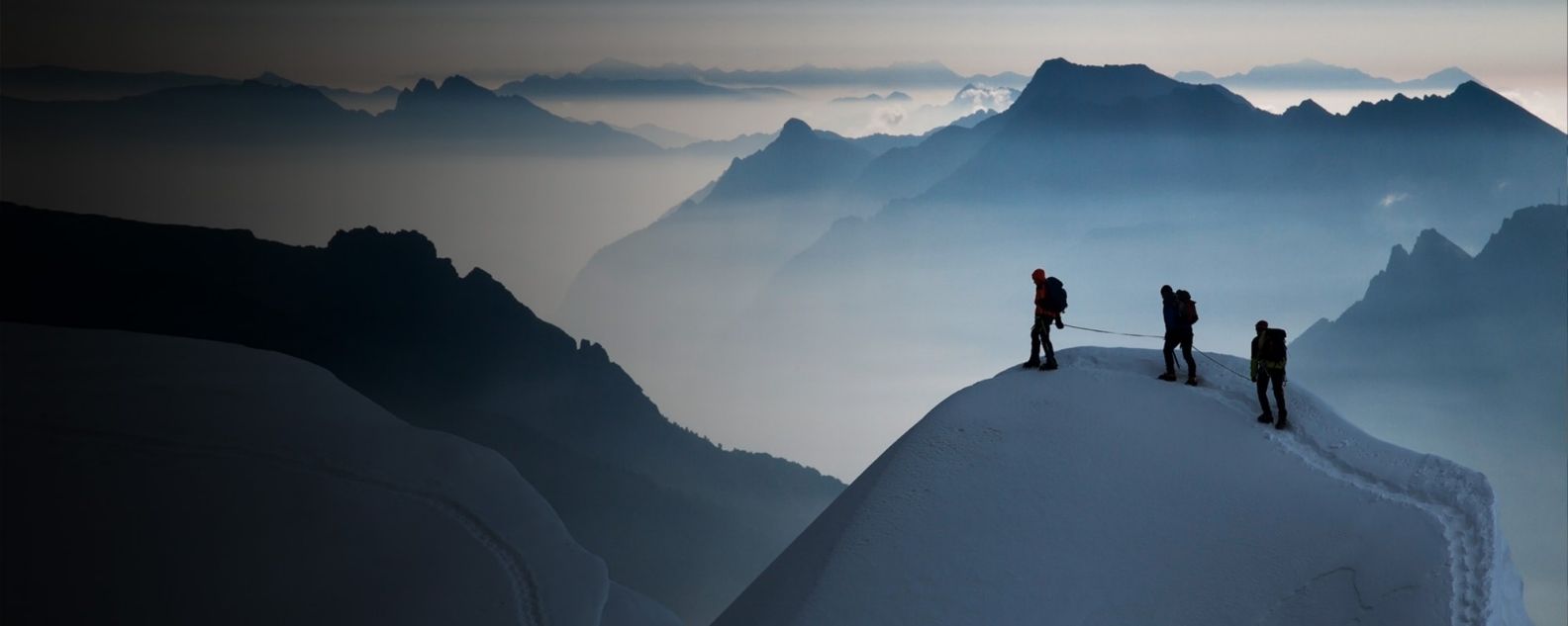 눈 덮인 산봉우리에 서 있는 세 명의 산악인 