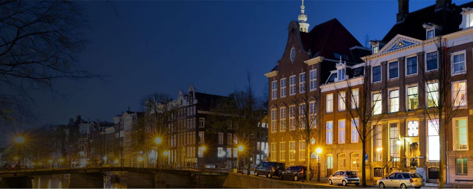 Foto de edificios tradicionales con coches estacionados en la orilla de una calle en Ámsterdam, Países Bajos.