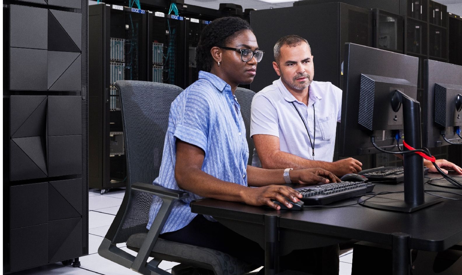 Two workers sitting in a server room working at a computer