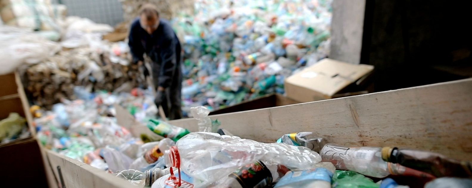 At a recycling factory, a worker pushes plastic bottles with a shovel for recycling
