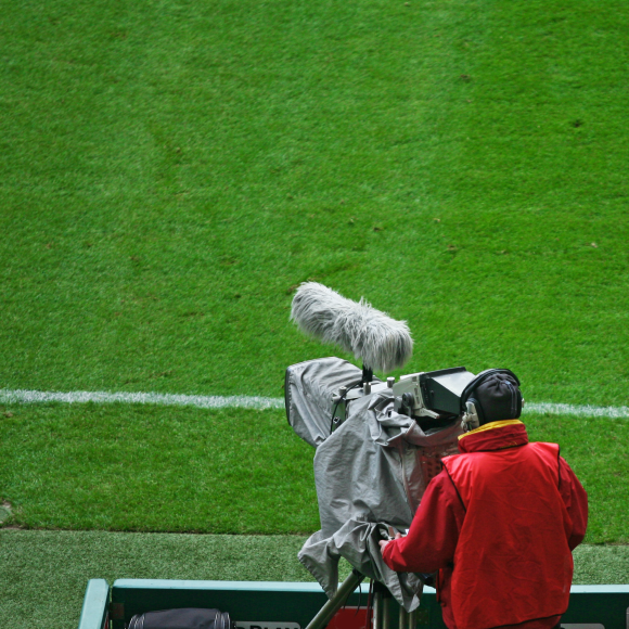 Vista posterior de hombre con cámara de televisión en campo deportivo