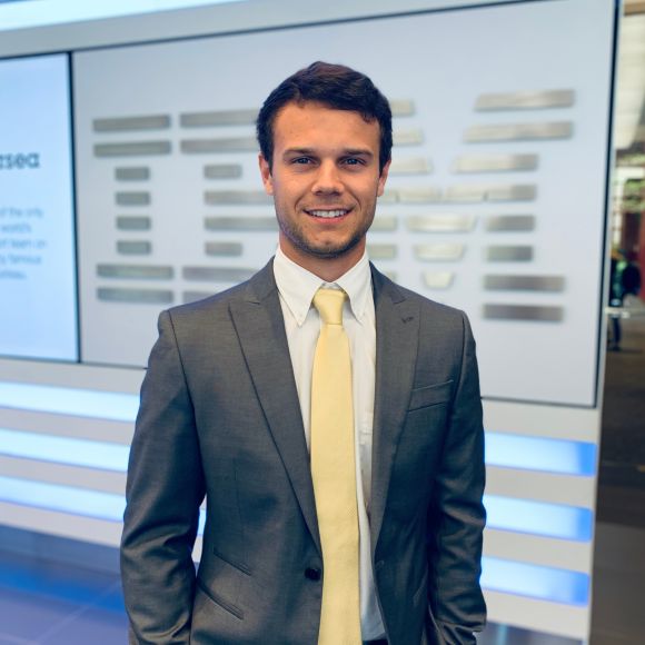 Employee wearing a suit and smiling in front of IBM sign