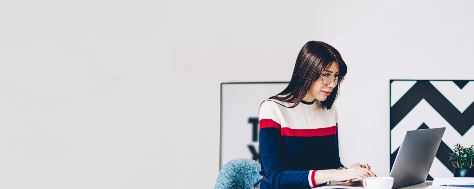 Giovane studentessa con gli occhiali che scrive informazioni per il corso di studio con la tastiera di un moderno laptop utilizzando una connessione internet wireless in un elegante appartamento