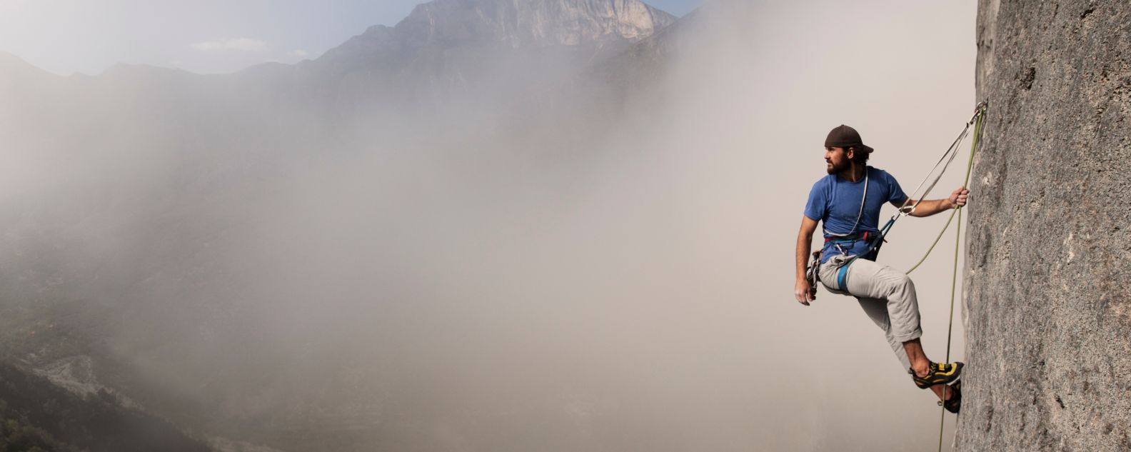 Mountain climber ascends a rock face among the clouds