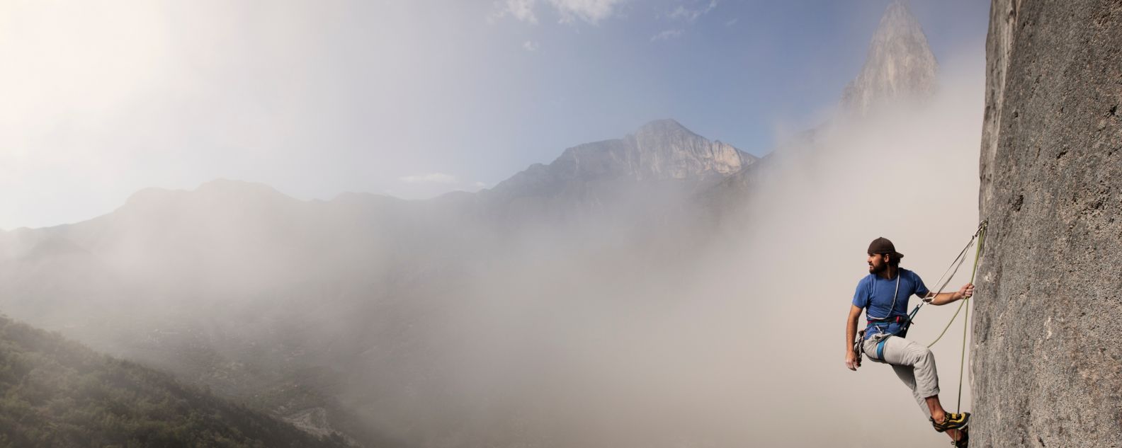 Mann allein, Nebel und Berge im Hintergrund, ruht sich auf seinem Aufstieg aus