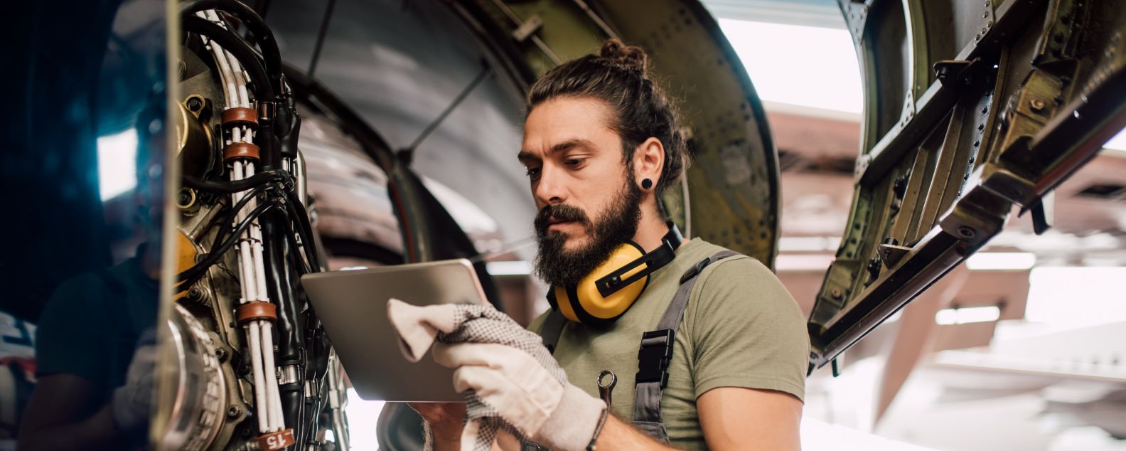 Seorang lelaki menggunakan tablet digital saat memperbaiki pesawat