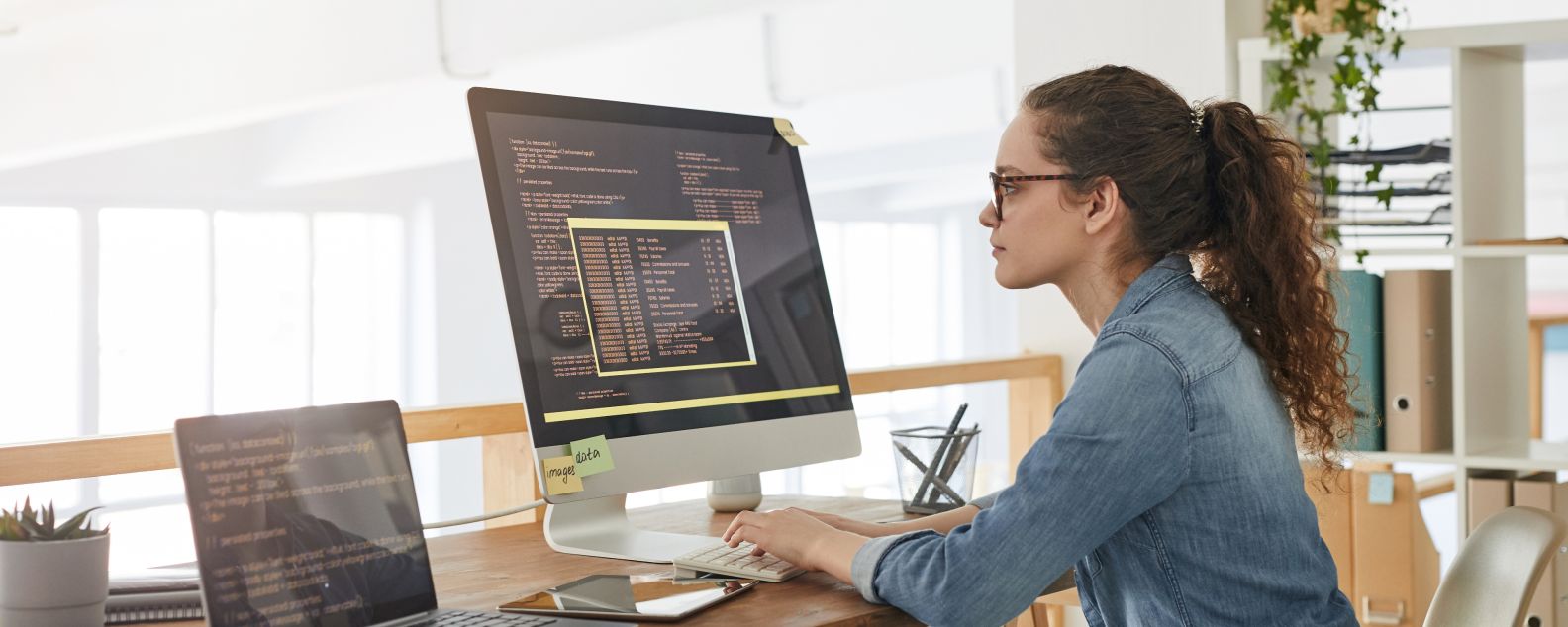Retrato de vista lateral de una desarrolladora de TI escribiendo en el teclado con código de programación negro y naranja en la pantalla de la computadora y la computadora portátil