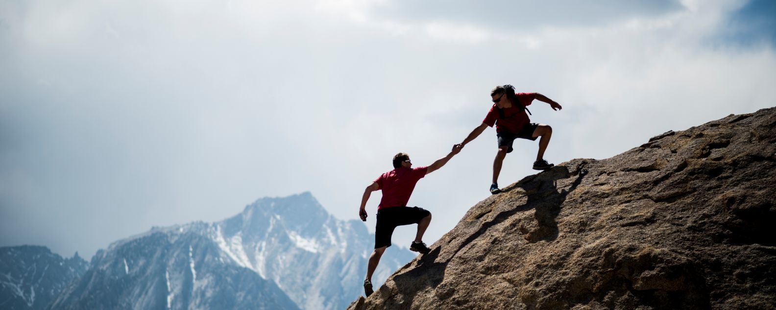 Un grimpeur en aide un autre à atteindre le sommet d’un rocher géant 