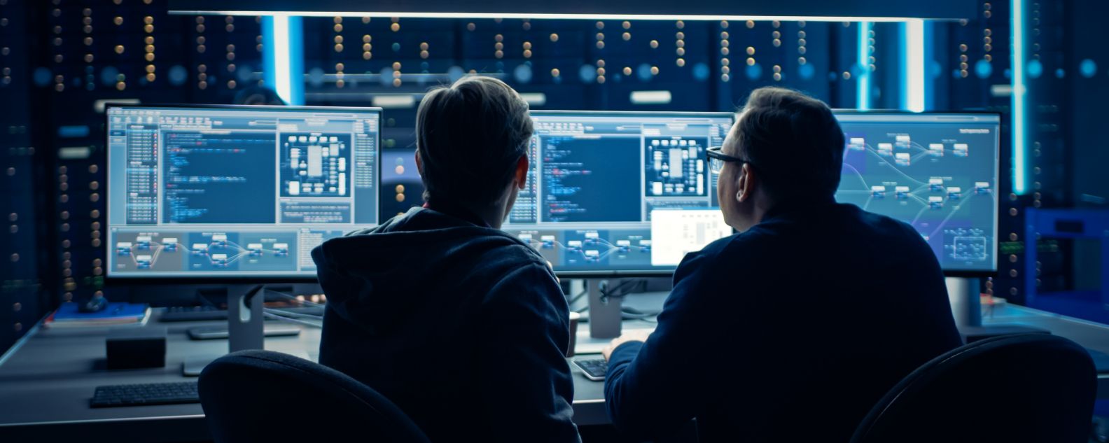 Two Professional IT Programers Discussing Blockchain Data Network Architecture Design and Development Shown on Desktop Computer Display. Working Data Center Technical Department with Server Racks