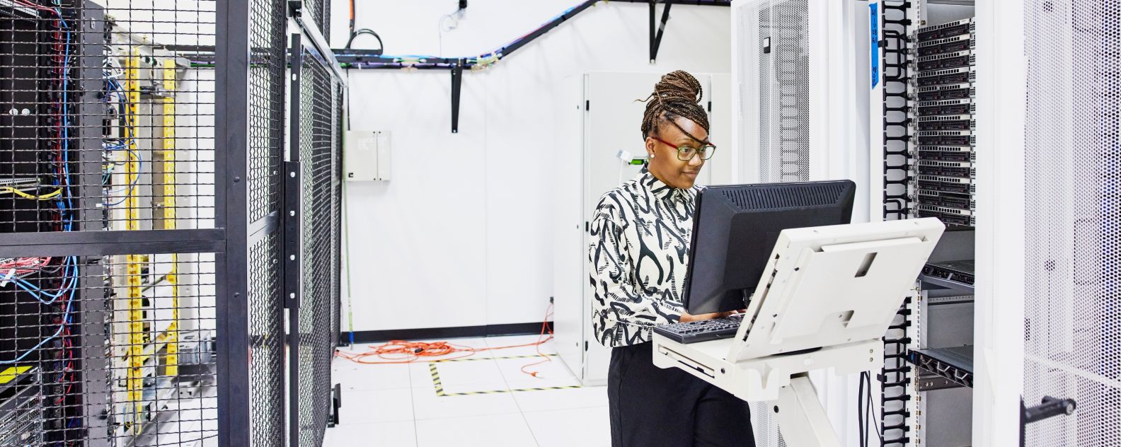 データセンターでサーバーの構成に取り組む女性IT担当者を広角撮影した写真。