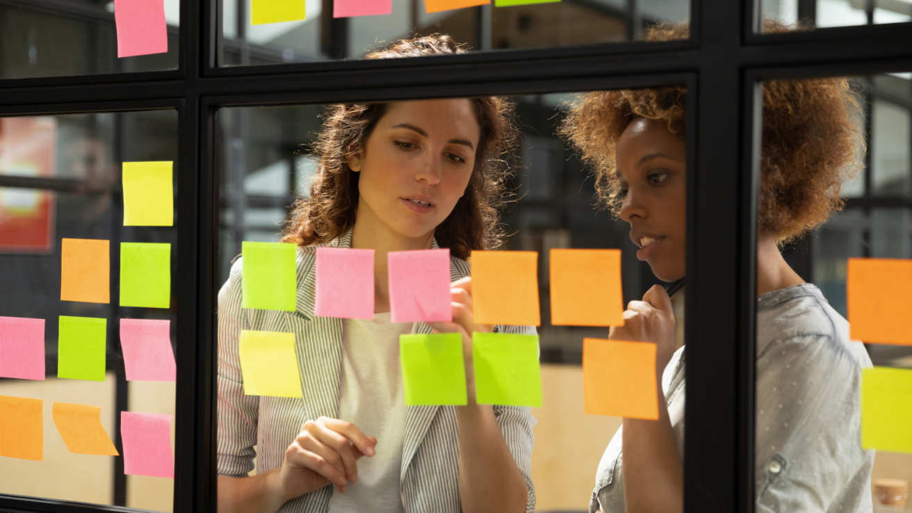 Collègues écrivant sur des notes autocollantes de couleur fixées à la fenêtre d'un bureau