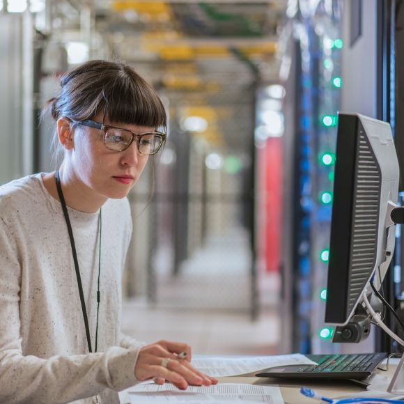 Person with glasses sitting at a computer in a data center